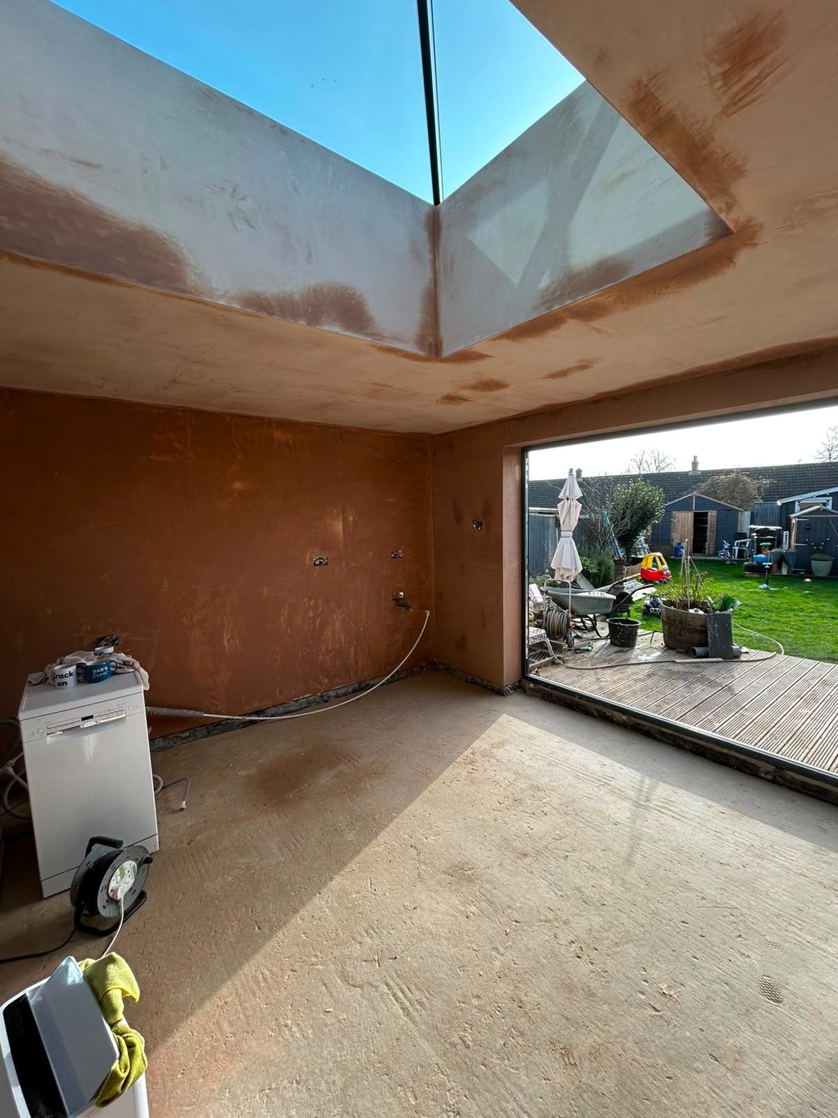 Freshly skimmed extension interior with pink plaster on walls and ceiling around a glass roof lantern.